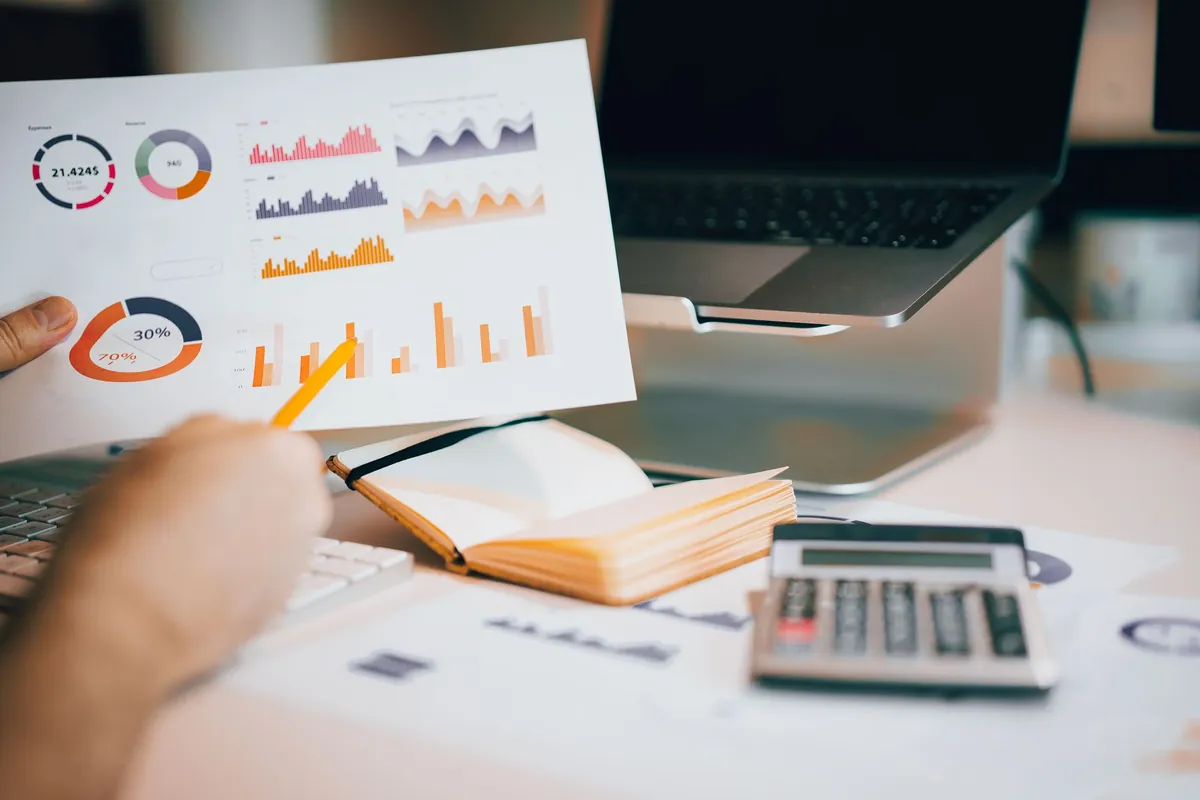 Printed charts, a calculator and a laptop on a dark desk