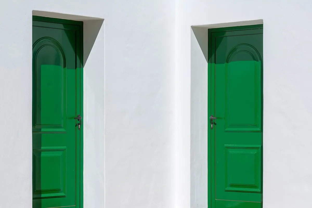 Two identical green doors set in a white wall