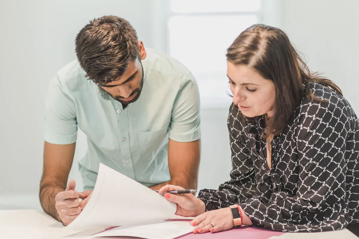 Two people leaning over printed pages together at a table