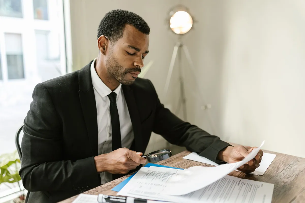 A man at a desk reading a paper document through a magnifying glass