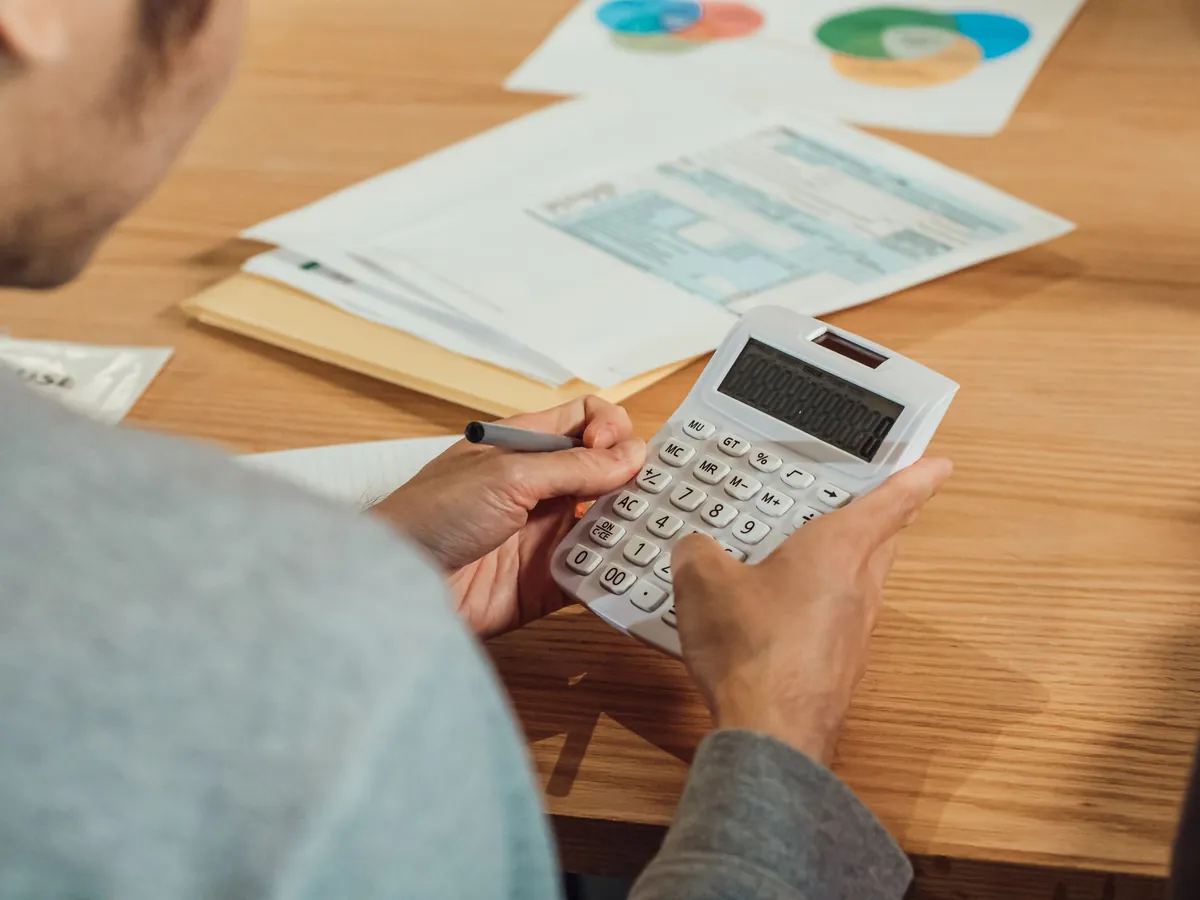 A person working a calculator at a desk with papers spread out