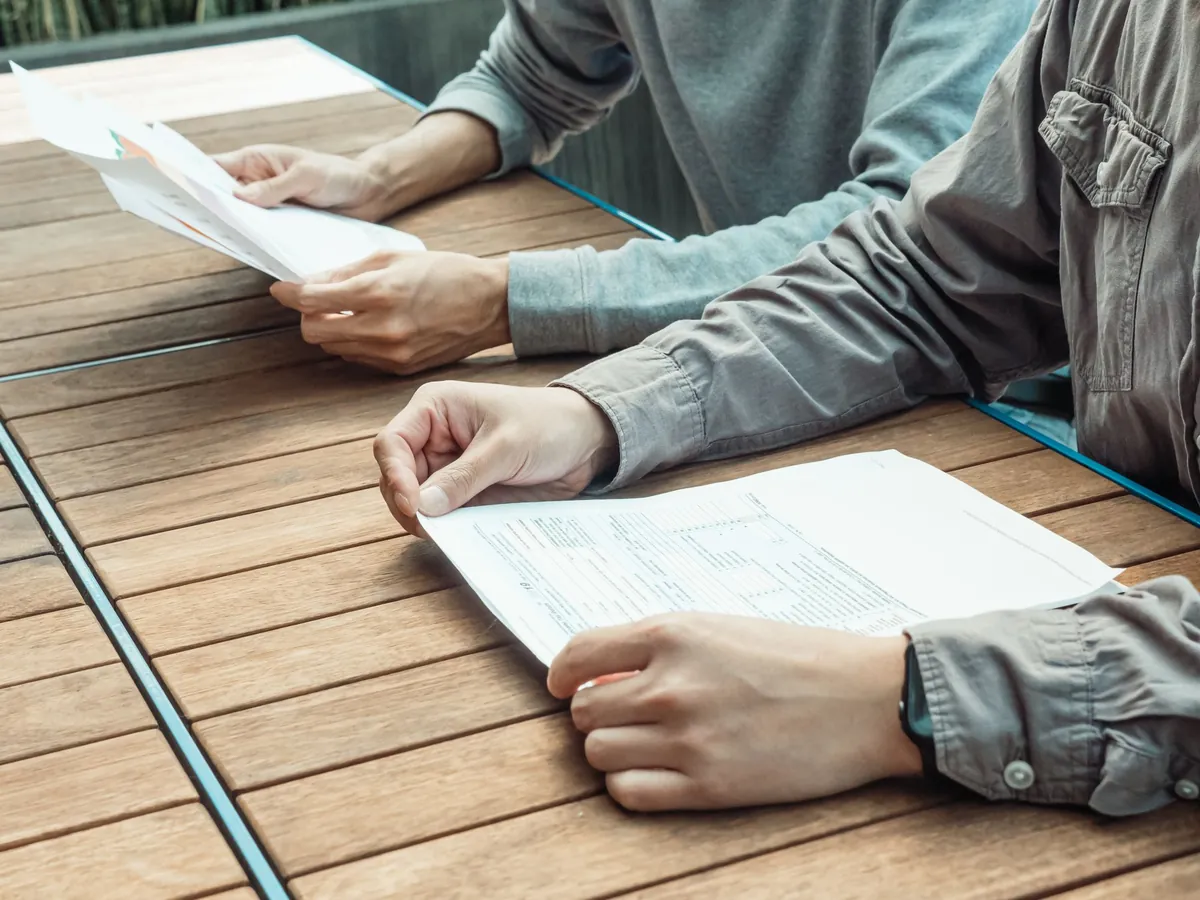 Overhead view of two people going through printed pages on a wooden table