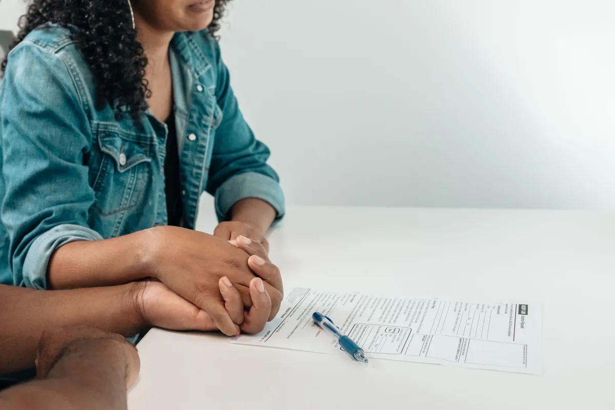 A person sitting at a white desk with a contract and a pen, hands folded