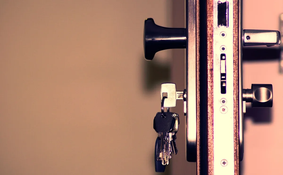 A small bunch of keys hanging from the barrel lock of a half-open apartment door, with the strike plate and handle in frame.