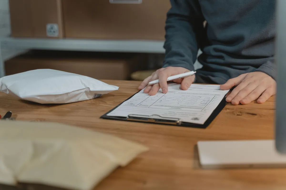 A person filling in a form on a clipboard at a wooden table