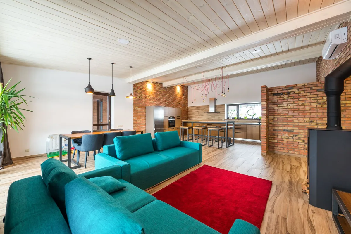 An open-plan living room with teal sofas, a red rug and a brick wall