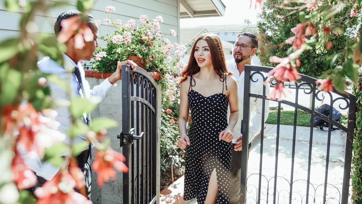 A man holding a garden gate open for two arriving guests