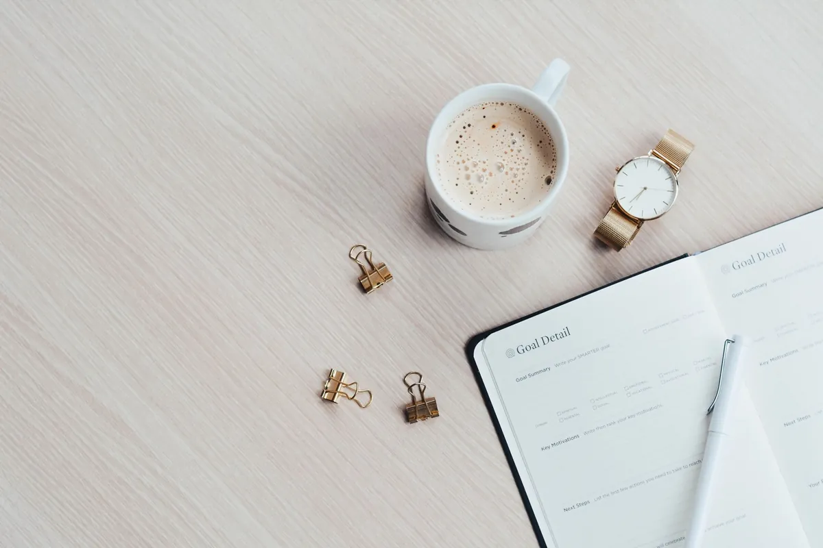 A tidy desk with a closed notebook, a pen and a cup of coffee