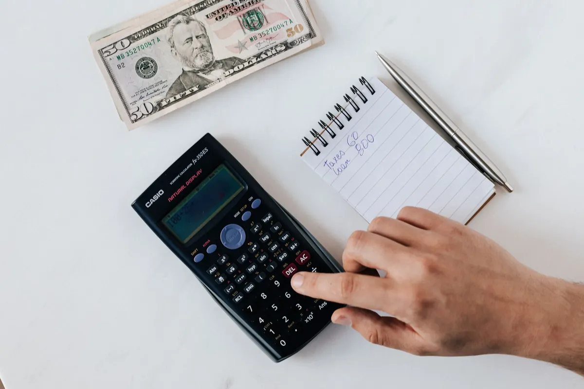 A desk seen from above with a calculator, a notepad and banknotes