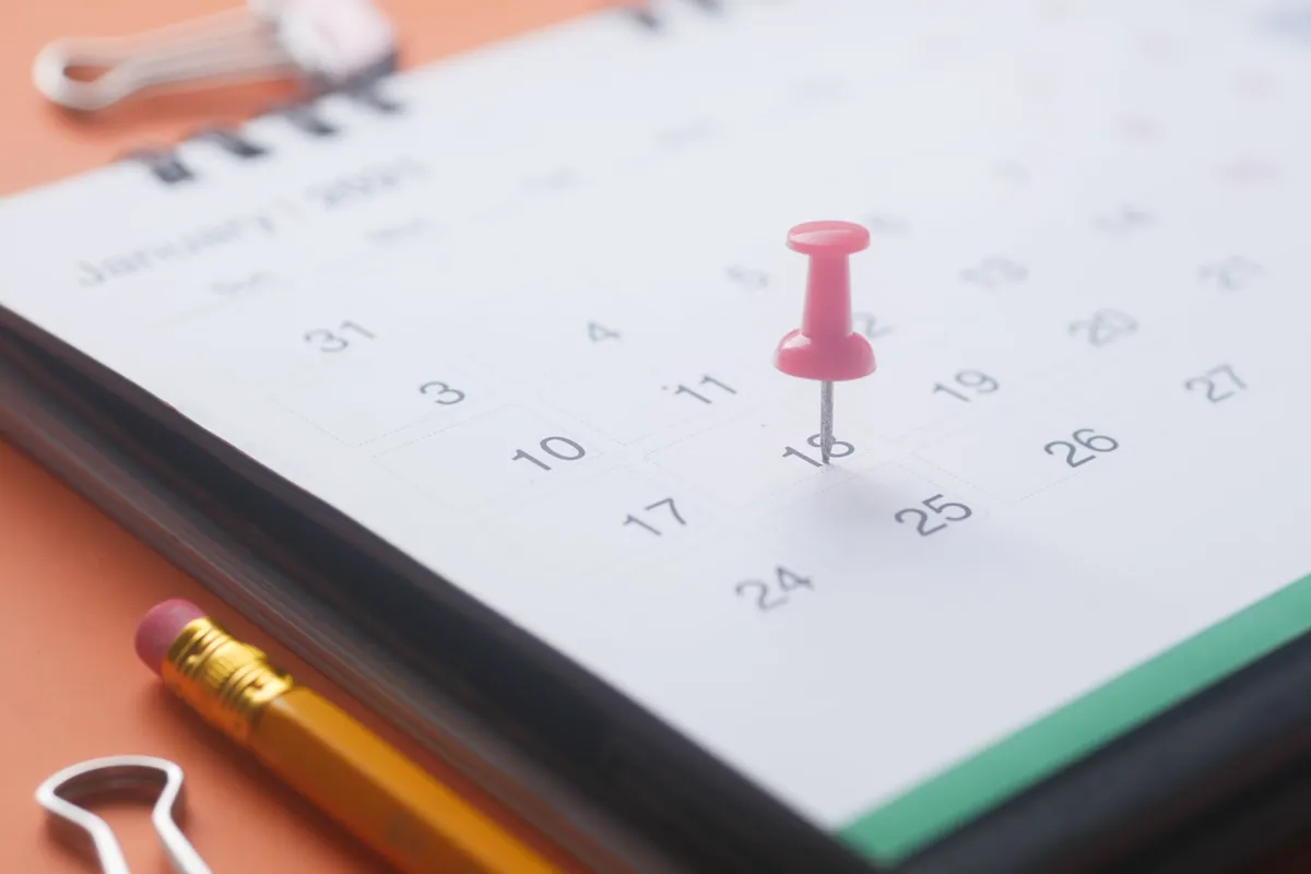 A red pin marking a date on a paper calendar beside a pencil