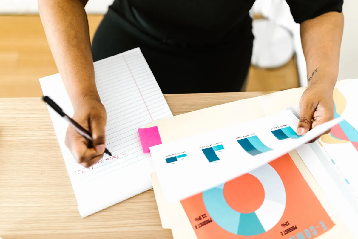 Two people reviewing colourful printed charts on a table, one holding a pen
