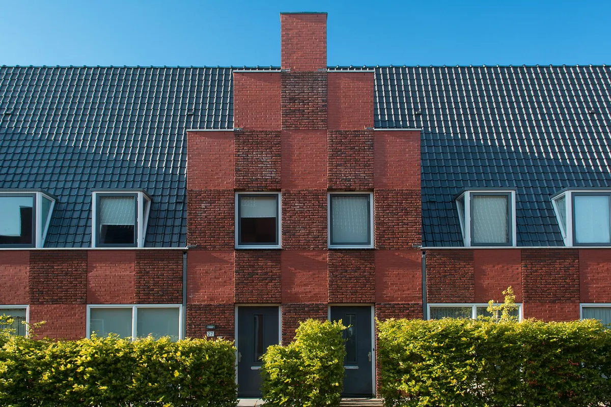 A row of red-brick townhouses with dormer windows behind a trimmed hedge