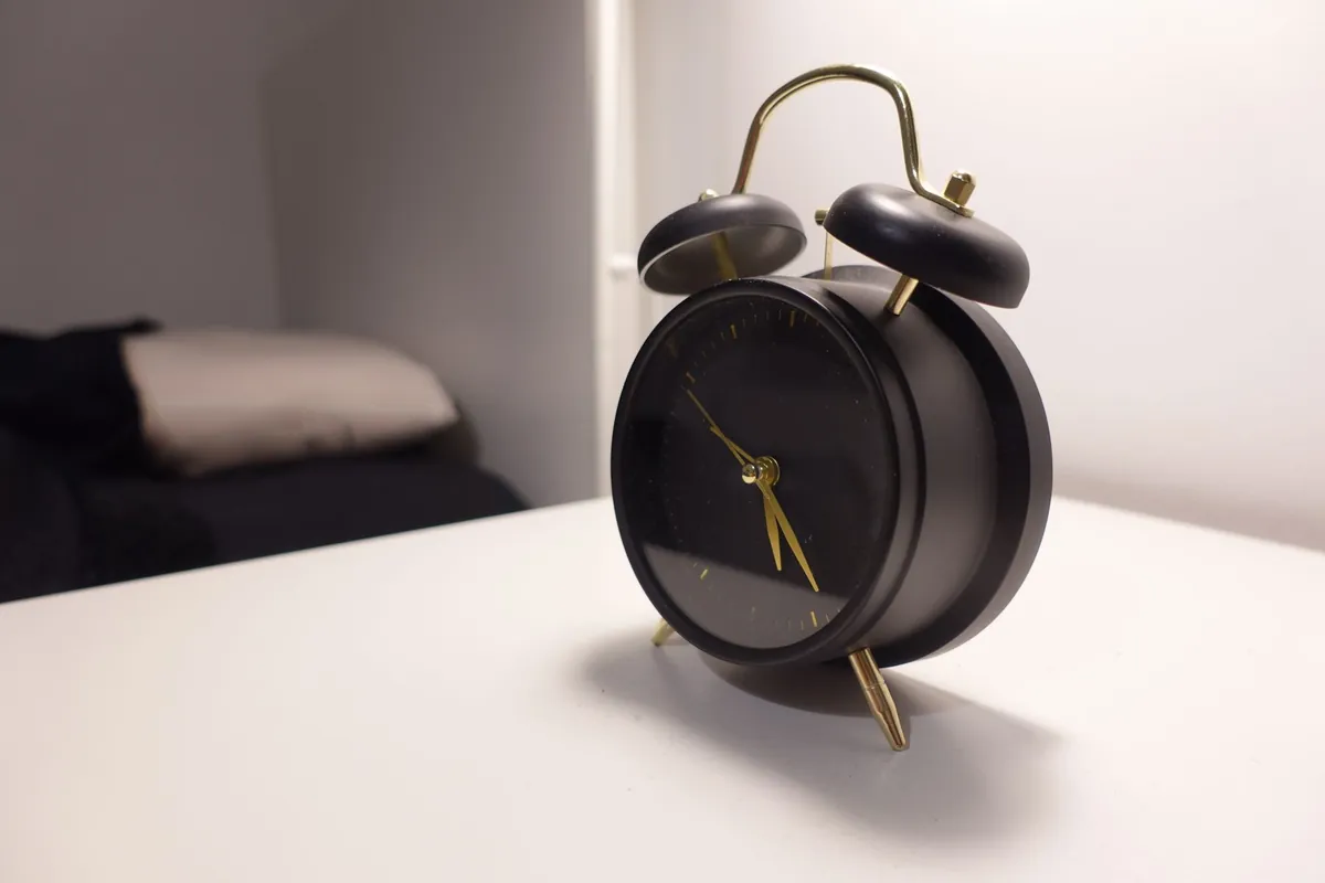 A black twin-bell alarm clock standing on a pale bedside surface