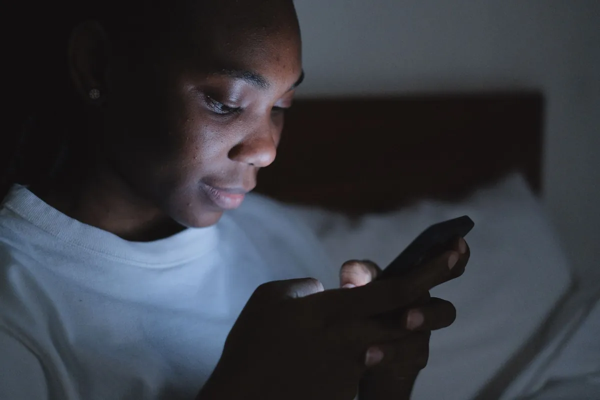 A man's face lit only by the screen of the phone he is holding in the dark