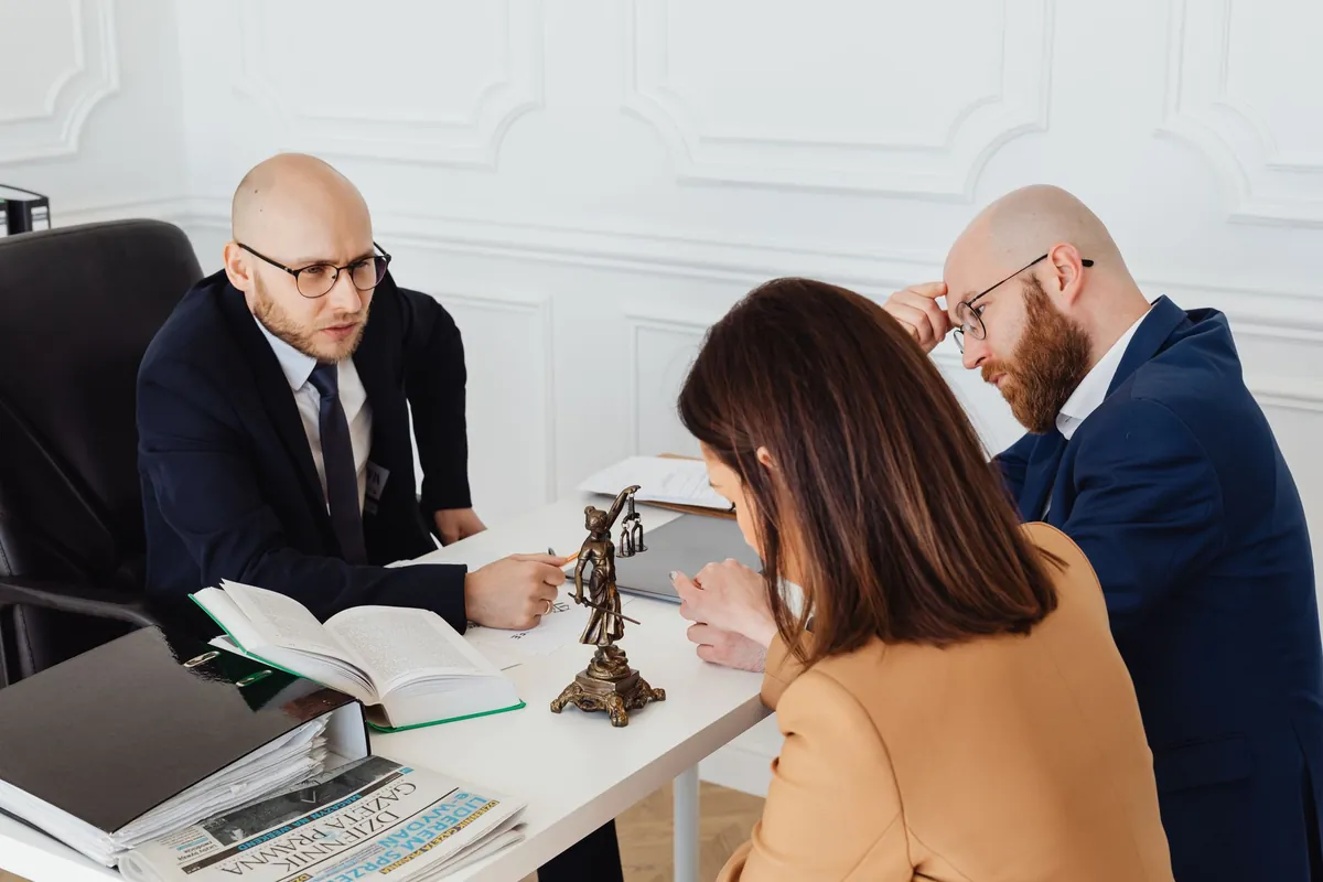 Three people at a table with open law books and a small statue of justice