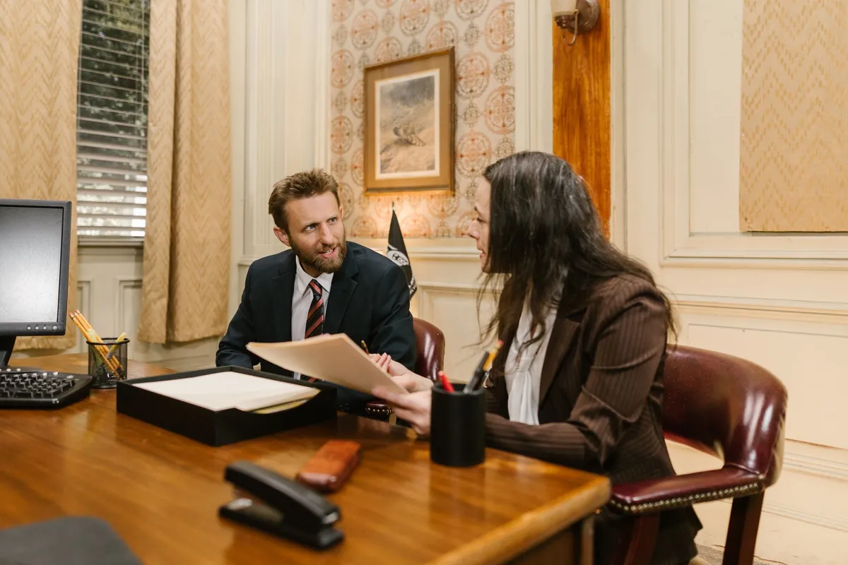 Two people going through documents at a desk in a wood-panelled office