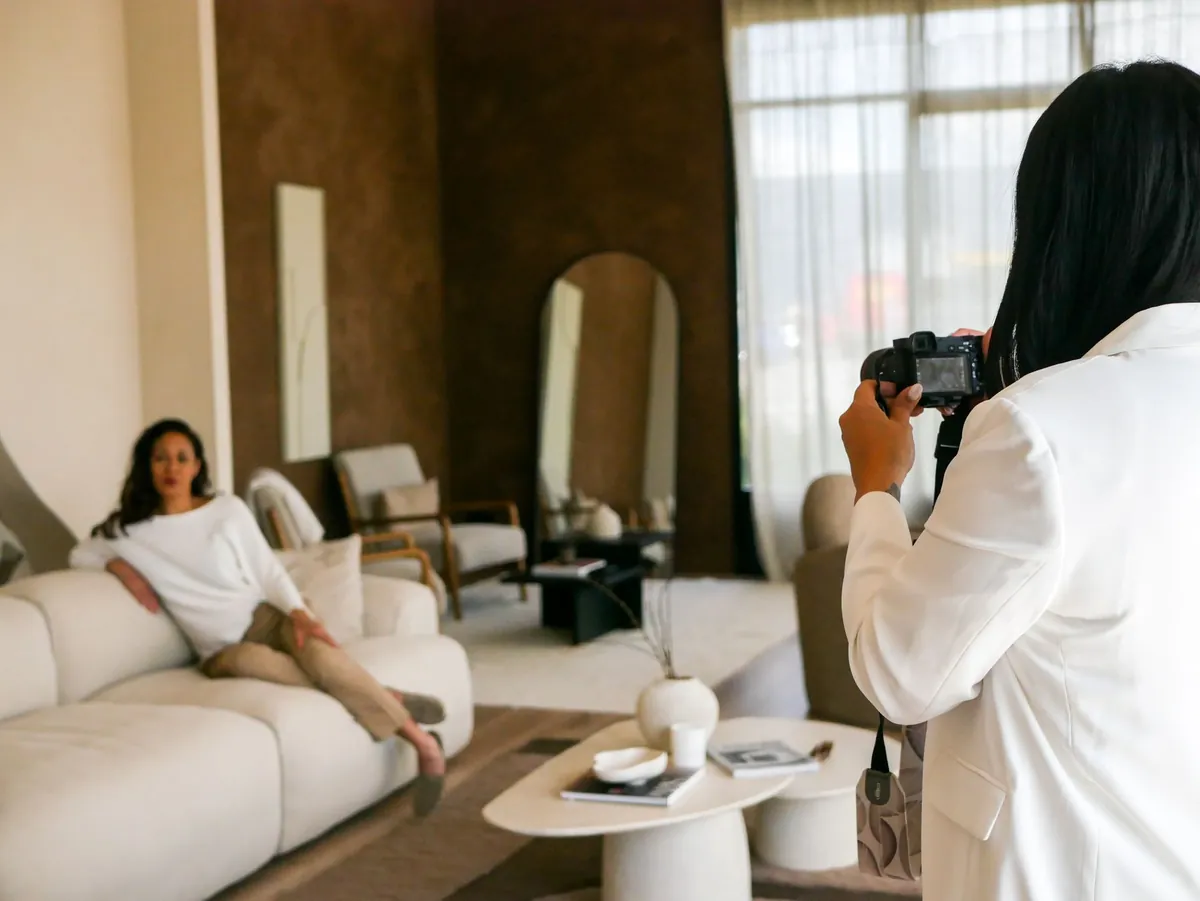 A photographer shooting a styled living room while a model sits on the sofa