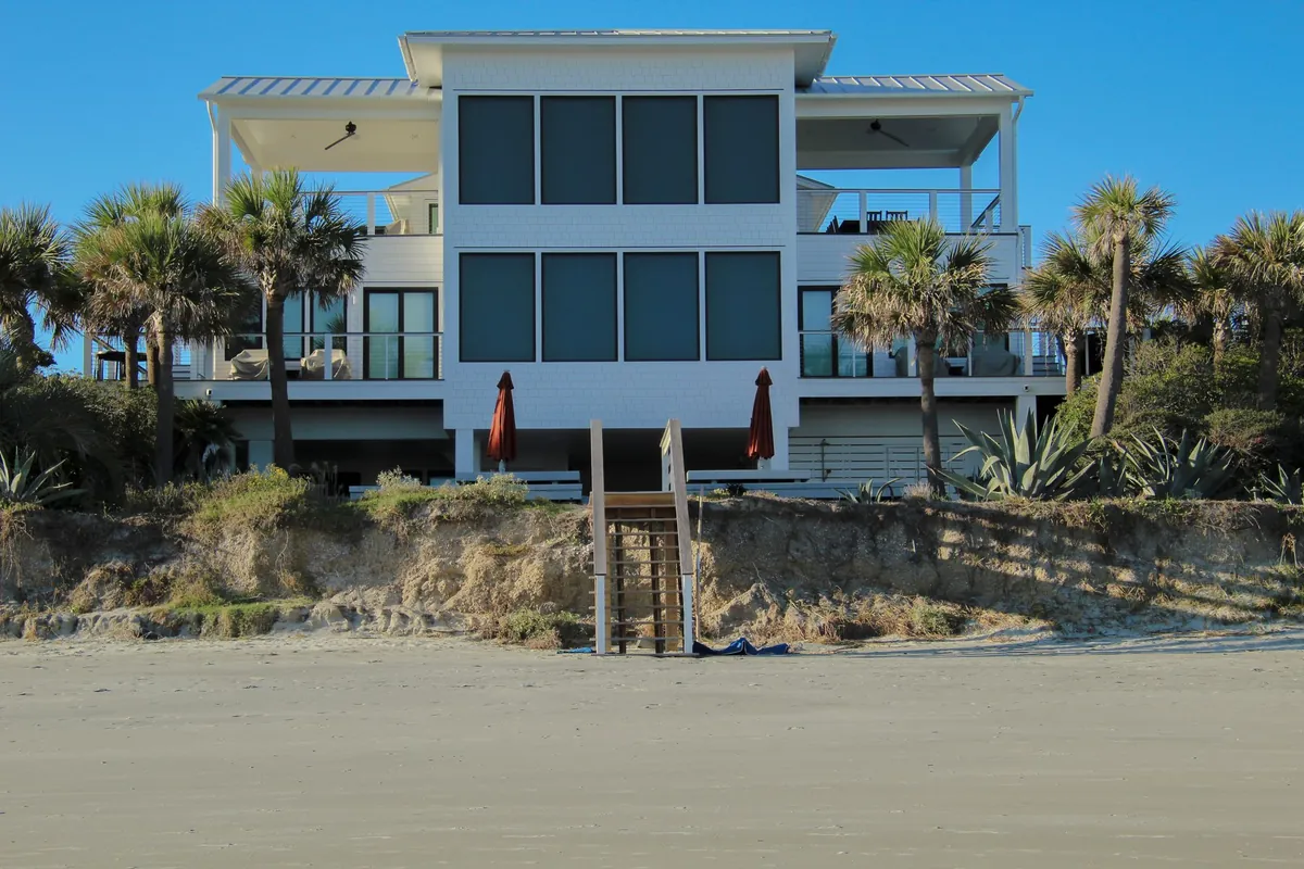 A modern beach house raised on stilts, seen from the sand