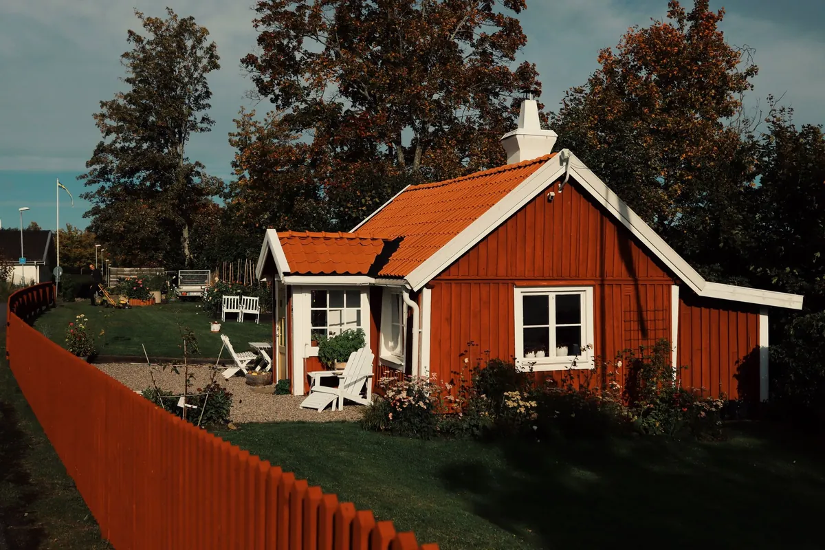 A red wooden cottage with white window trim in a summer garden