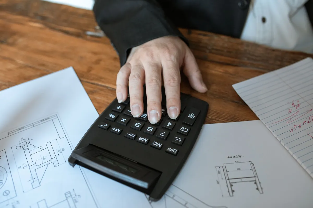 A hand working a calculator resting on technical drawings
