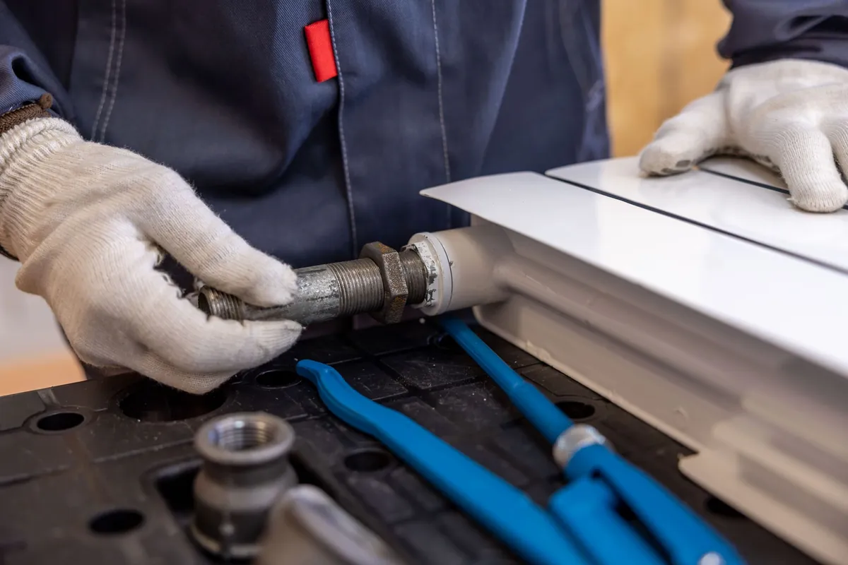 A worker in gloves fitting a pipe to a radiator
