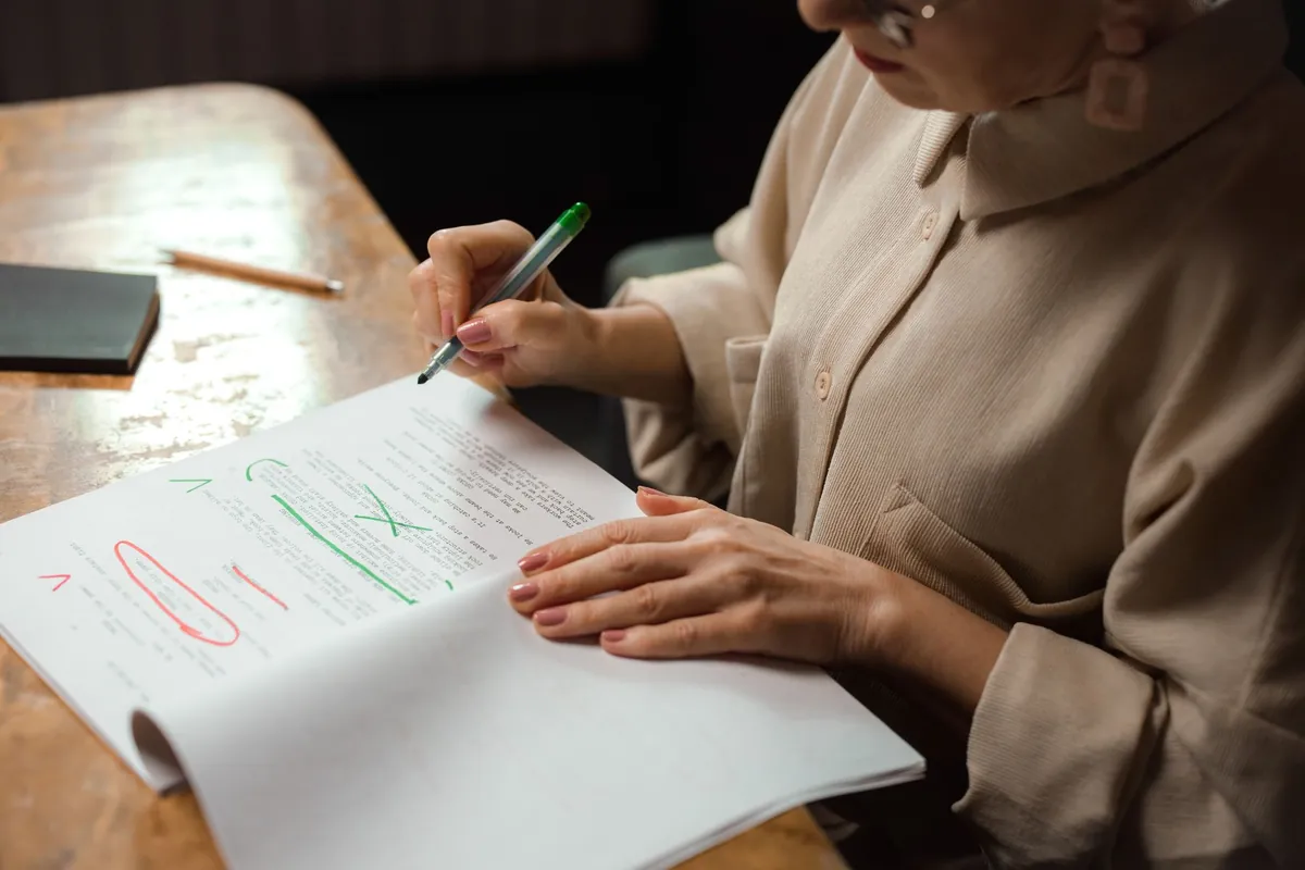 A woman marking corrections on a printed page with a red pen