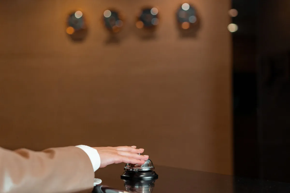 A hand pressing a small brass bell on a reception counter
