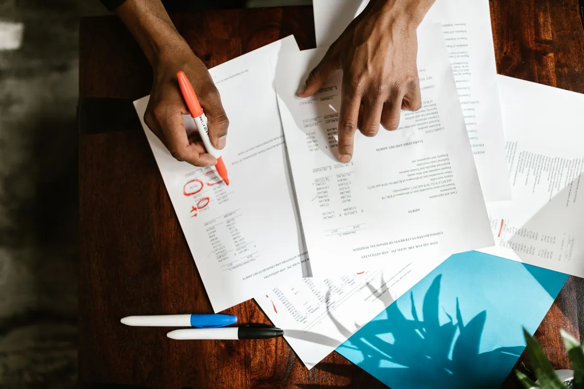 Hands marking printed statements with a red highlighter