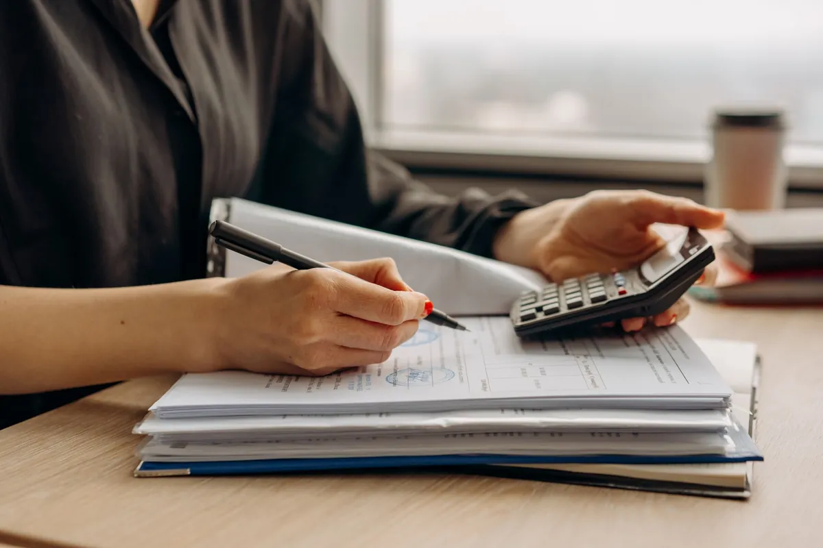 A person at a desk working a calculator beside an open folder