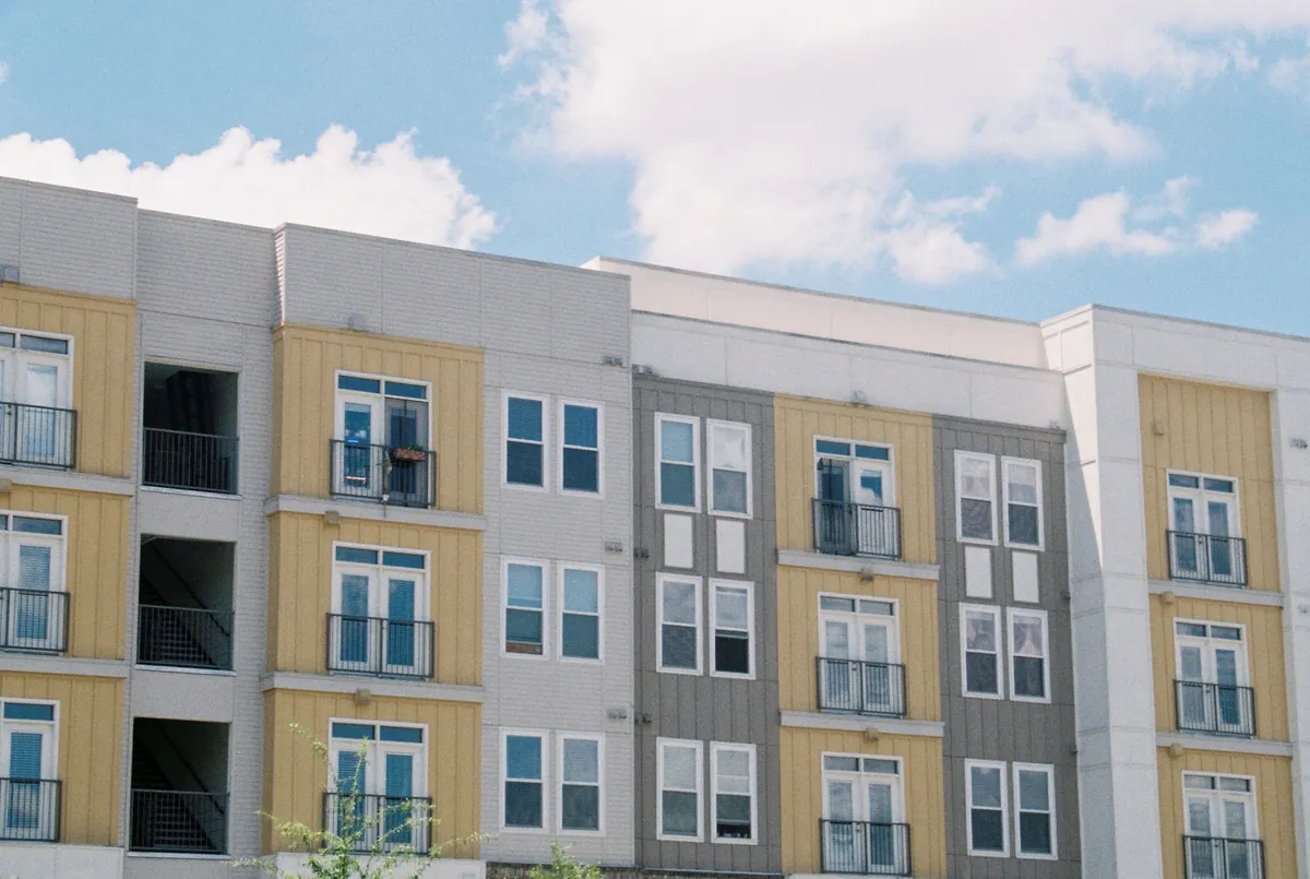 A low-rise apartment block in yellow and grey under a blue sky