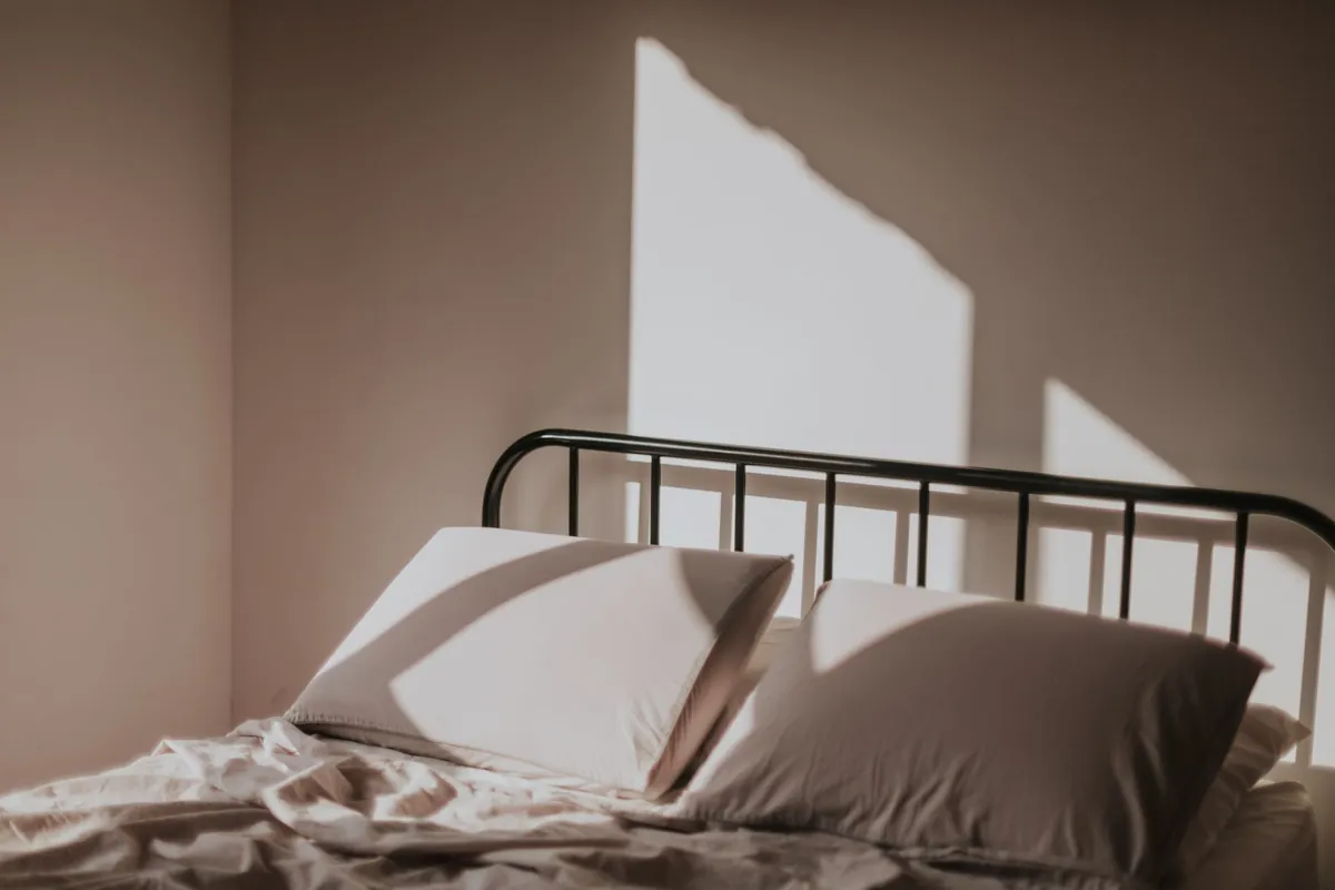 Morning light falling across a neatly made bed with a metal frame