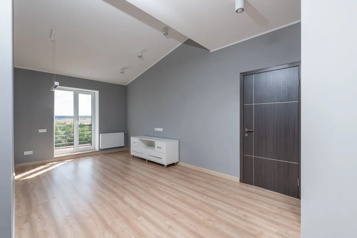An empty apartment with a wooden floor, grey walls and a closed dark door