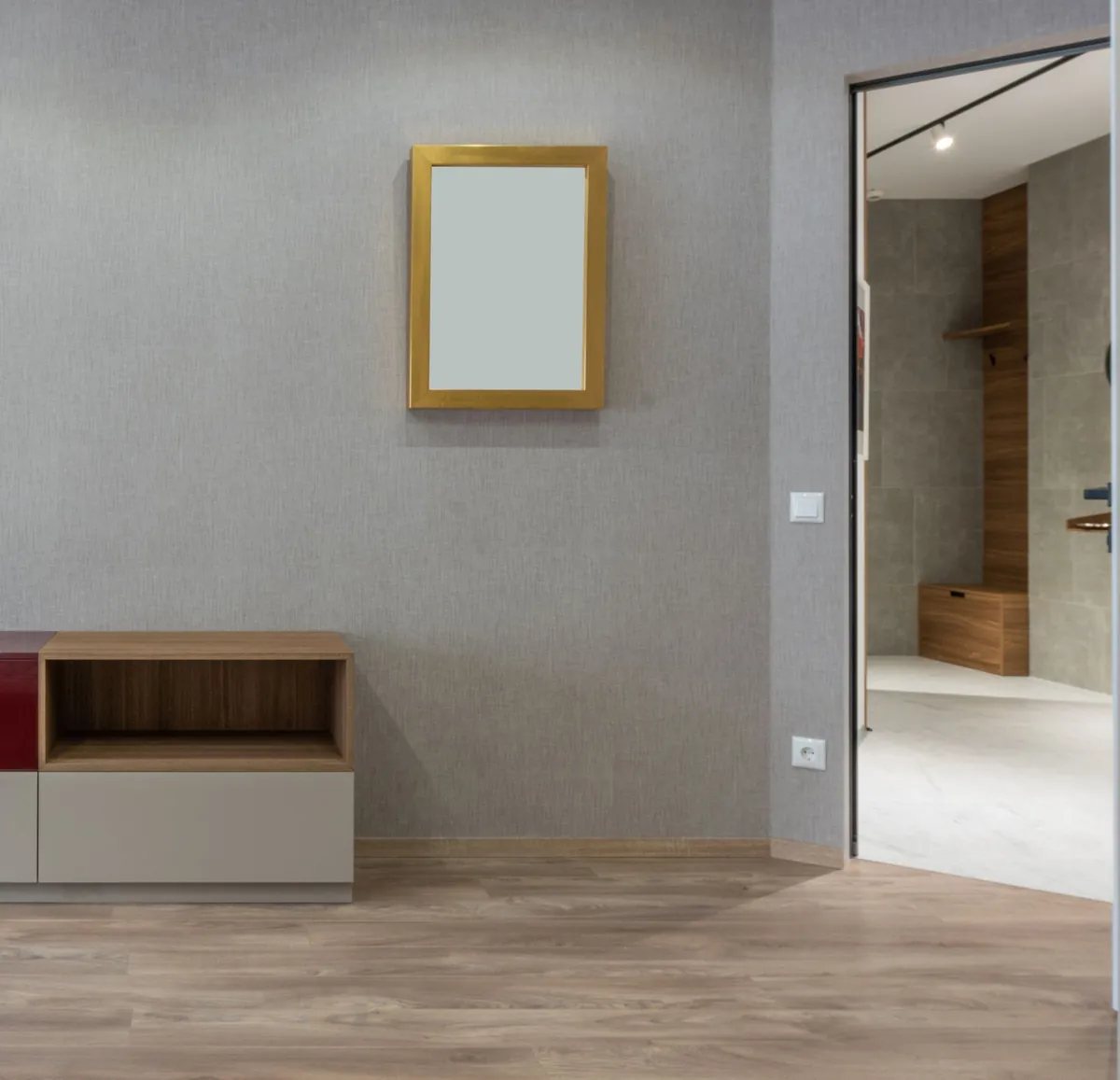 An empty room with a gold-framed mirror and a low cabinet, a door open to the next room