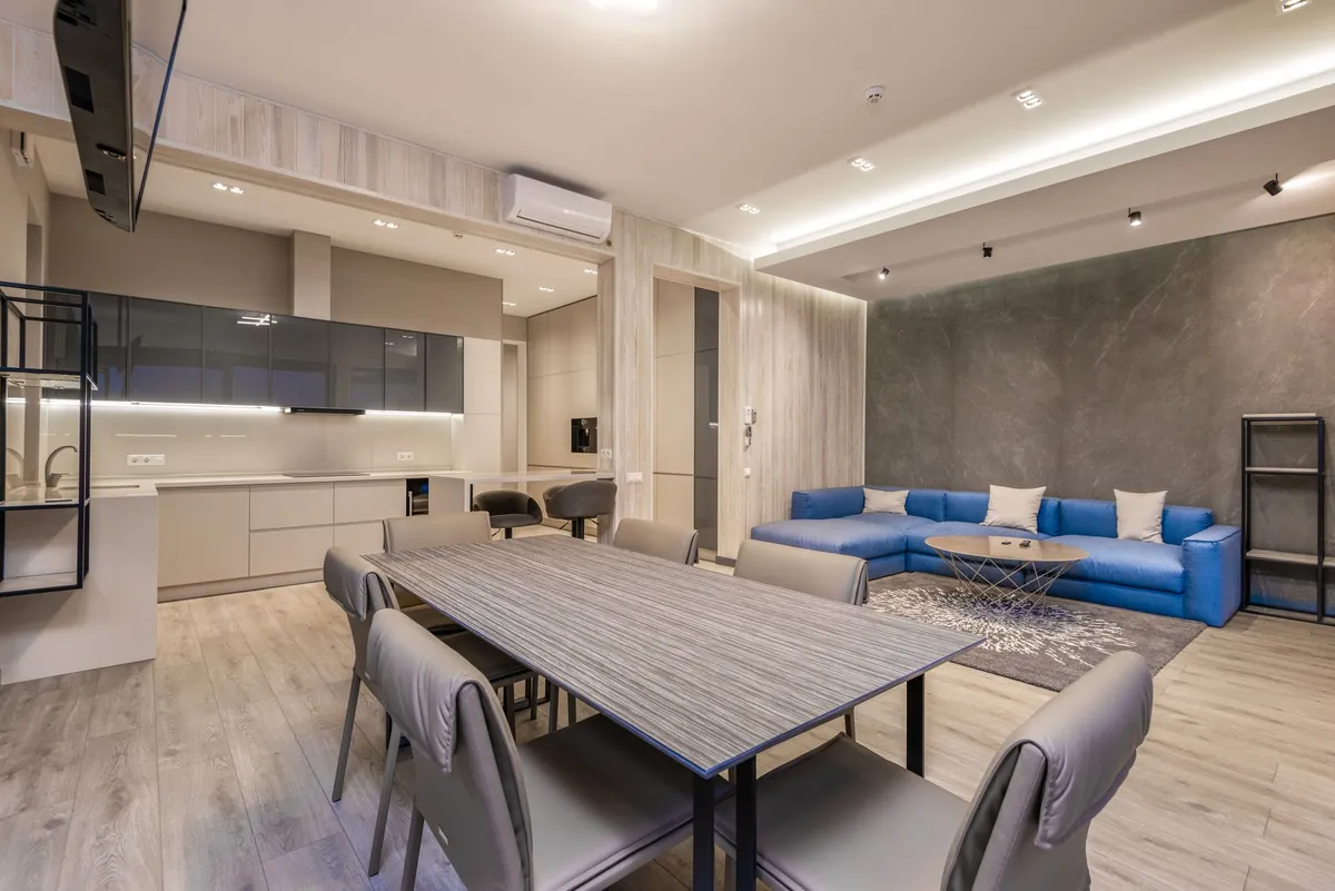 An open-plan furnished apartment with a dining table and a blue sofa