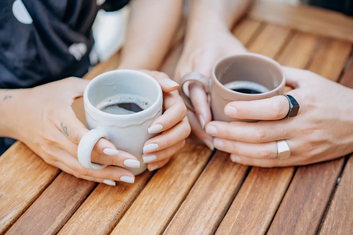 Two people holding mugs across a wooden garden table