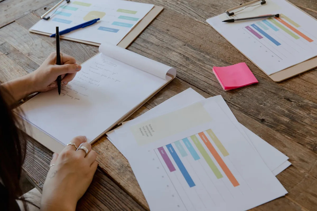 Hands writing on paper beside printed charts with colour-coded bars