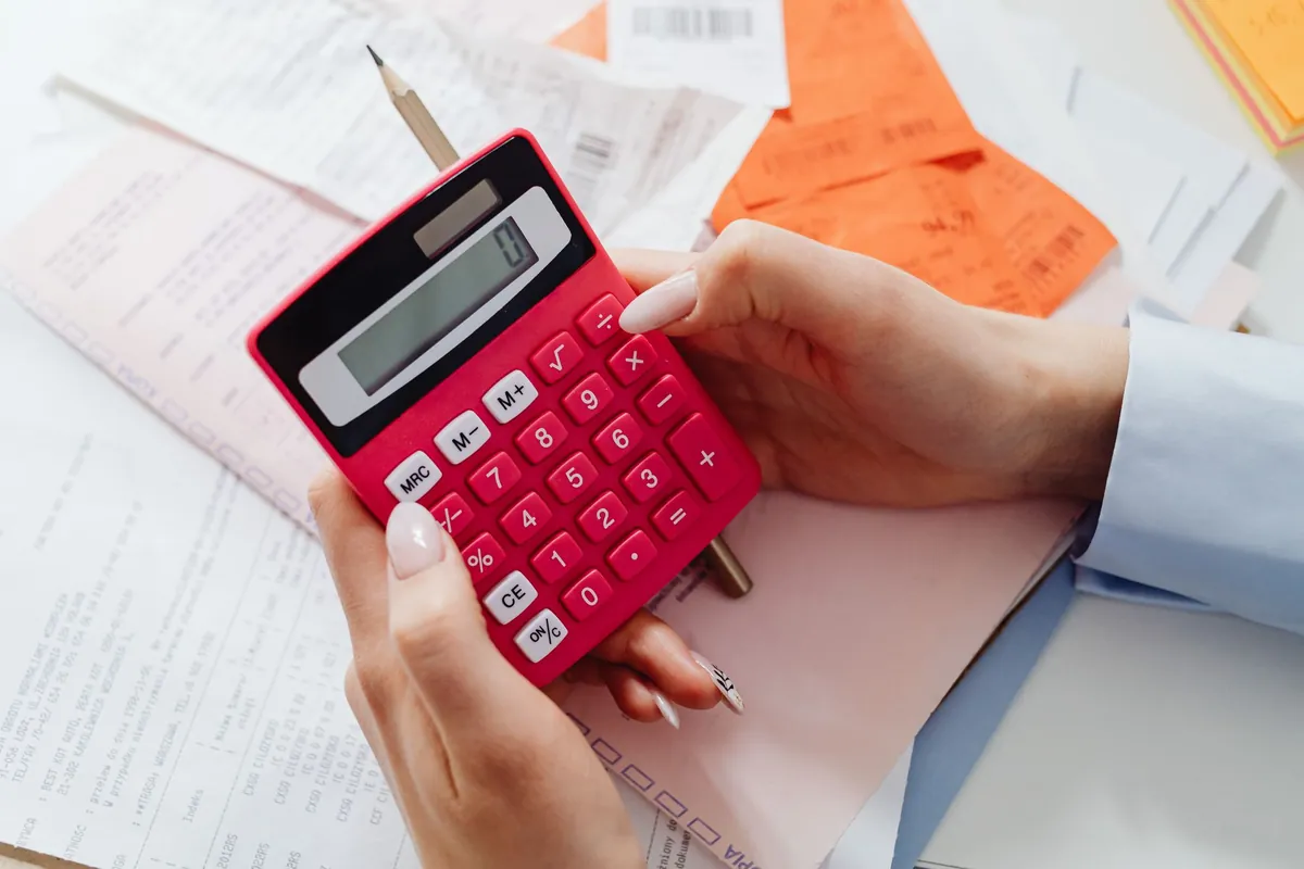 Hands working a red pocket calculator over a pile of printed statements