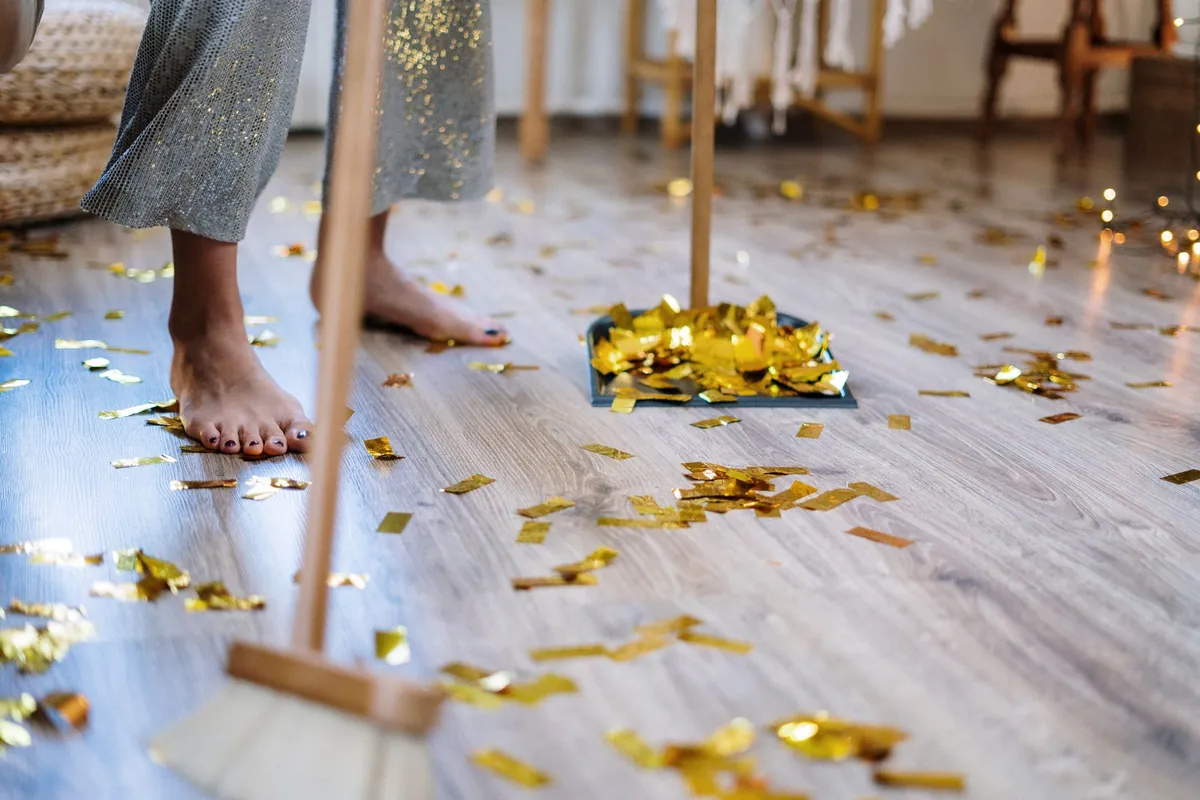 Someone sweeping gold confetti off a wooden floor