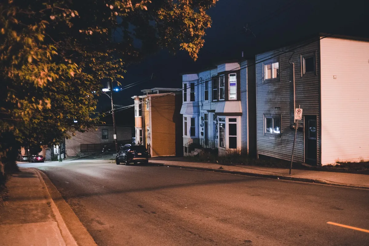 A quiet residential street at night with parked cars and lit houses