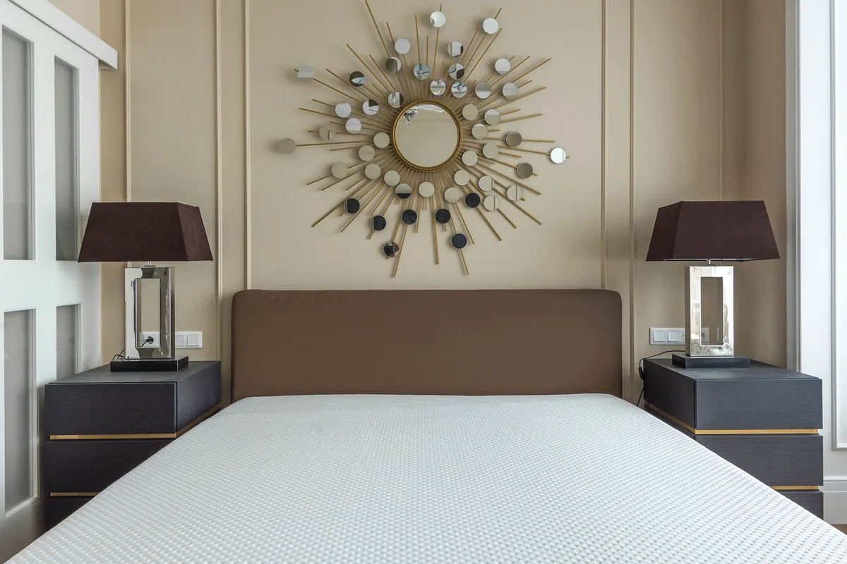 A stripped mattress on a bed between two lamps under a sunburst mirror