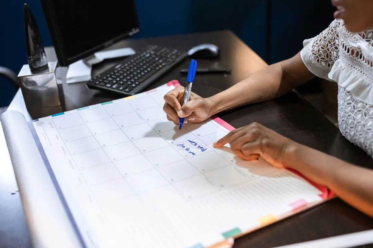 A host marking dates by hand on a blank month planner at a desk