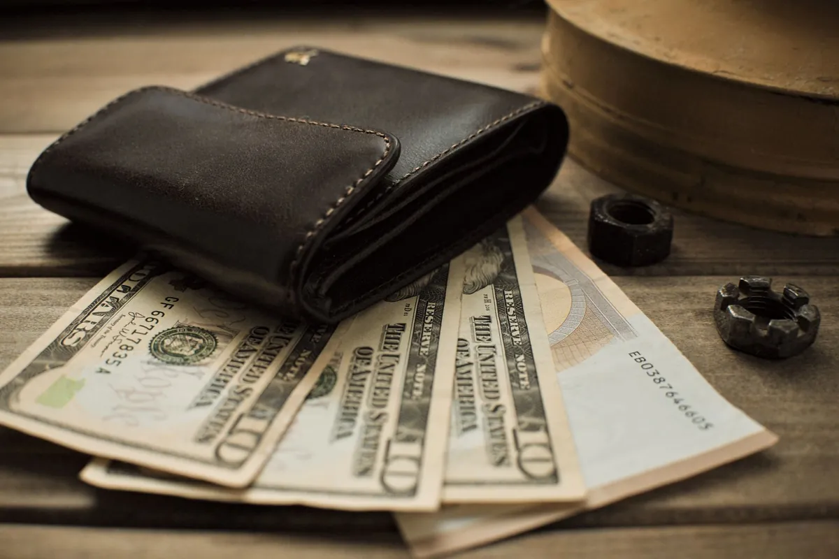 A leather wallet lying on a fan of dollar notes