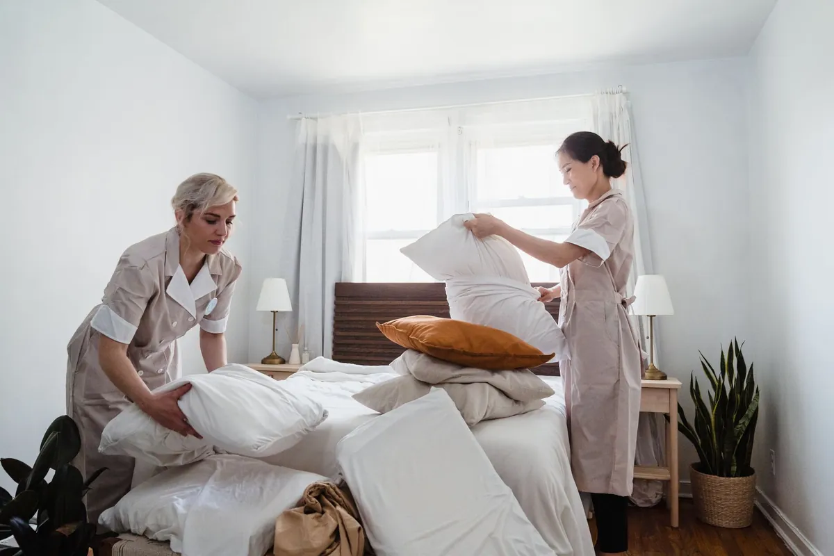 Two housekeepers in uniform making up a bed in a bright room