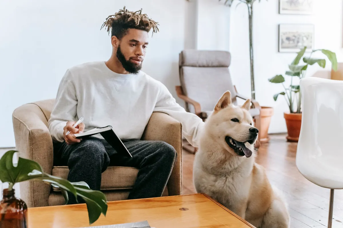 A man with a notebook in an armchair, a dog sitting beside him