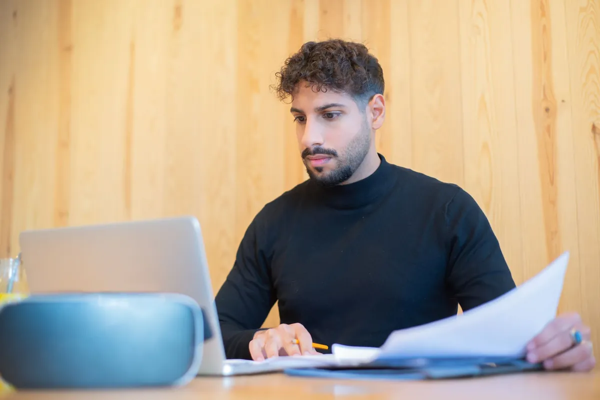 A host at a laptop with printed papers beside it, working through a written case