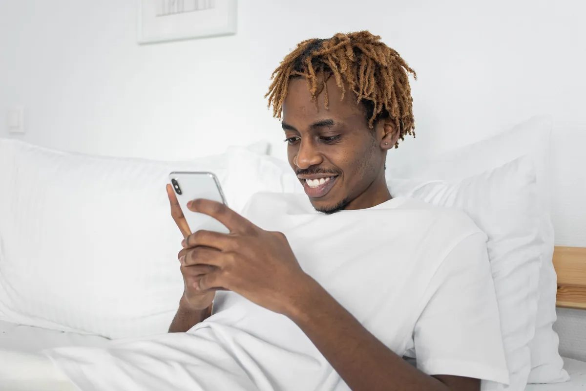 A guest lying in bed with white linen, smiling at a phone screen