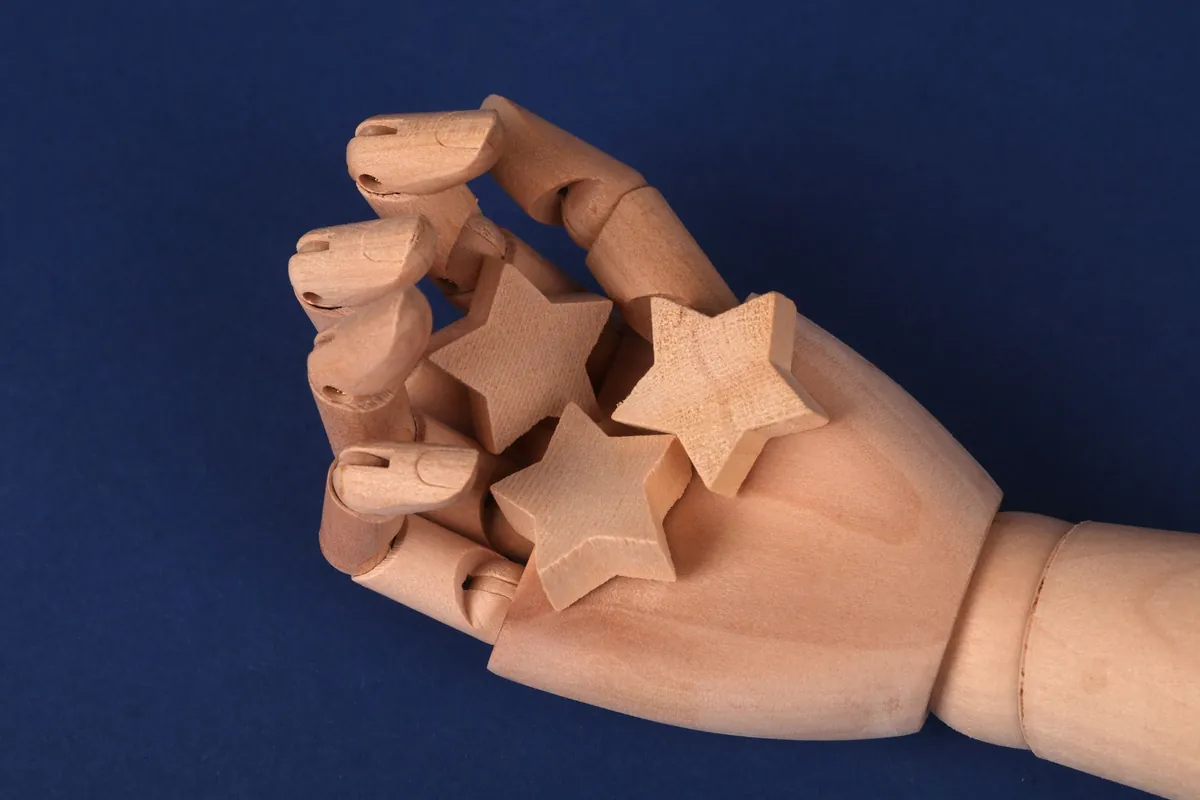A wooden artist's hand holding several small wooden stars against a navy background