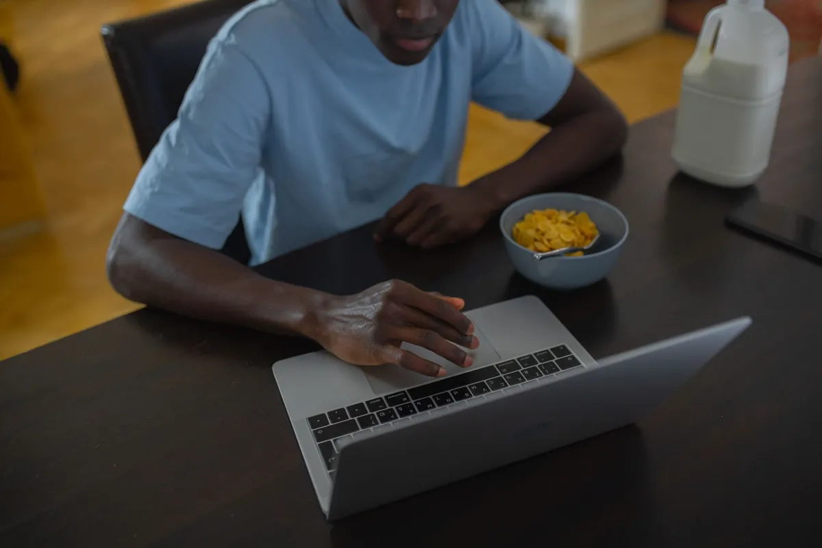 A man typing on a laptop at a breakfast table