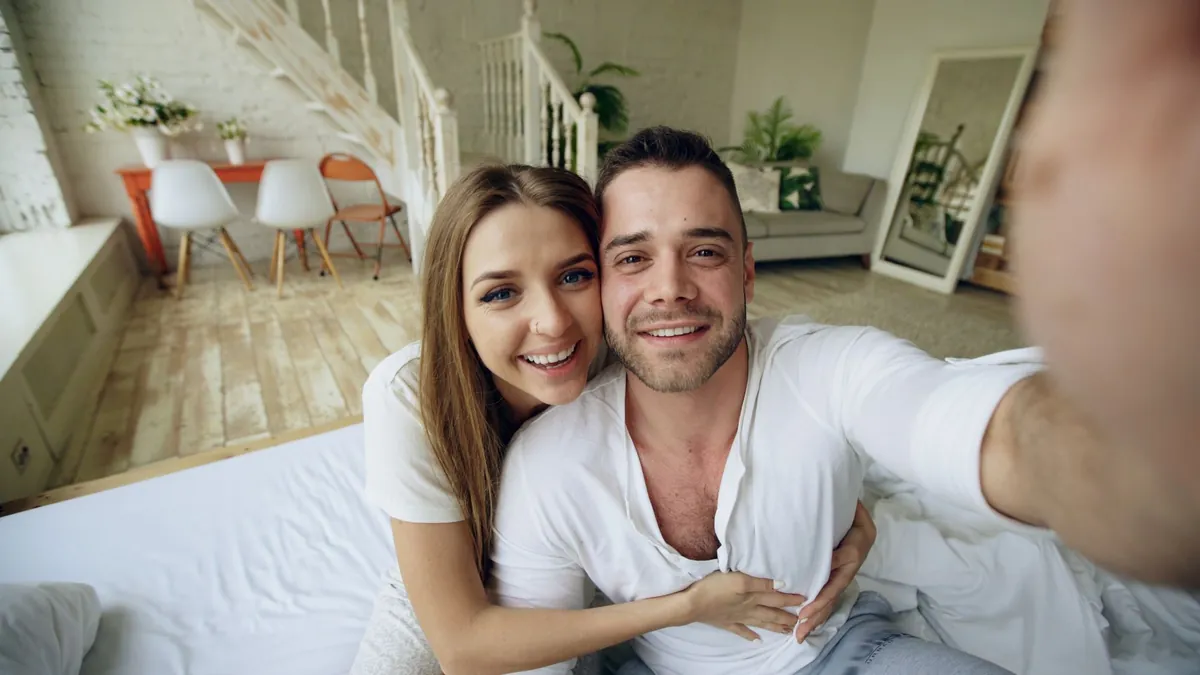 A smiling couple taking a selfie in a bright, comfortable room