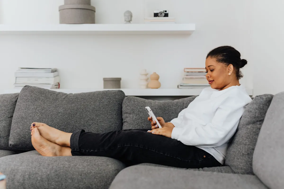 A woman sitting in a bright living room looking at her phone